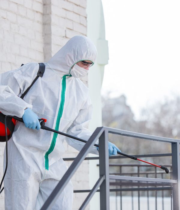 Coronavirus Pandemic. A disinfector in a protective suit and mask sprays disinfectants in the room. Protection of COVID-19 disease. Prevention of spreding pneumonia virus with surfaces we touch.